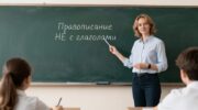 Учитель русского языка объясняет пятиклассникам правило правописания НЕ с глаголами у школьной доски